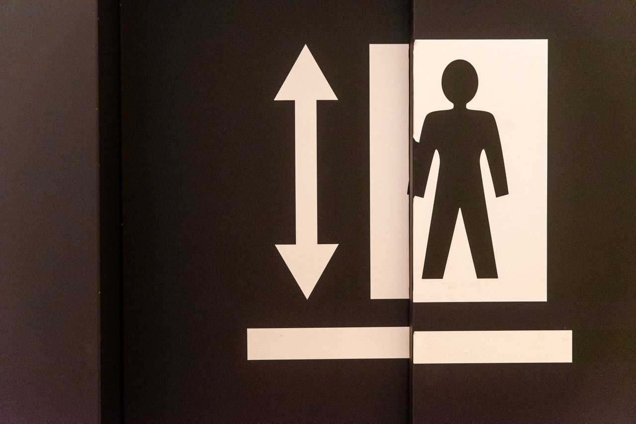 Graphic of an elevator door with a human figure and directional arrow symbol.