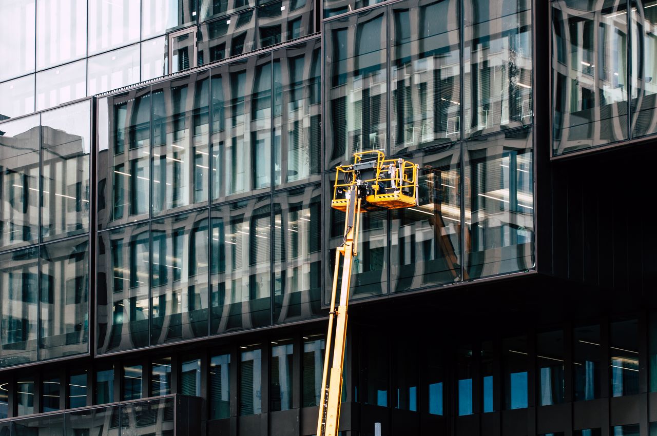 Workers on a lift cleaning windows of a modern glass building exterior.